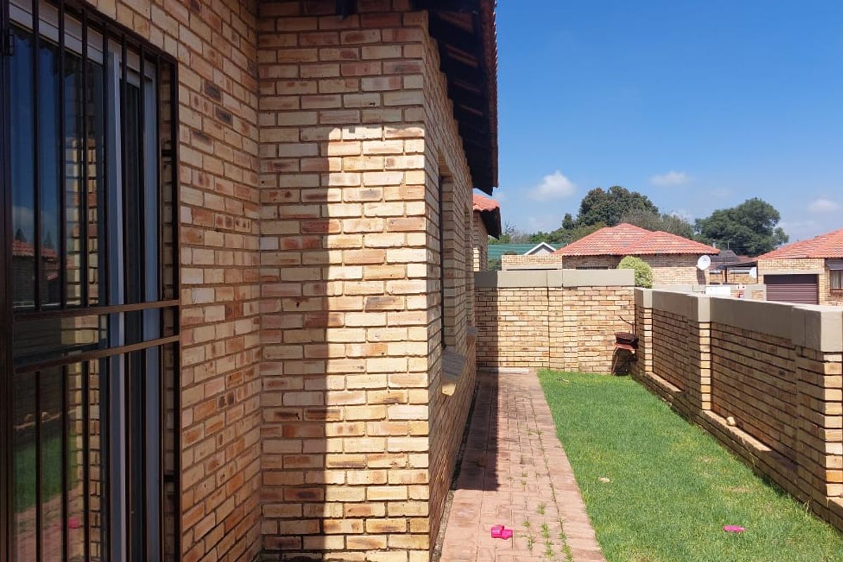 A view of the rear exterior of the townhouse, featuring face brick walls, a paved walkway, and a private garden area with boundary walls.