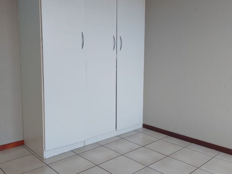 A simple, empty bedroom featuring neutral tiled flooring and a built-in white wardrobe with ample storage space.