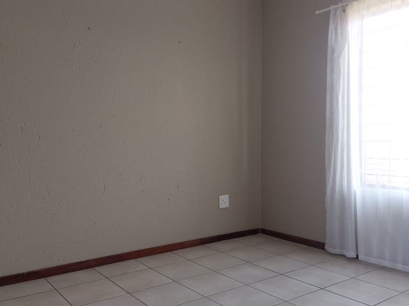 A bright, empty bedroom featuring neutral-toned walls, tiled flooring, and a window fitted with security bars.