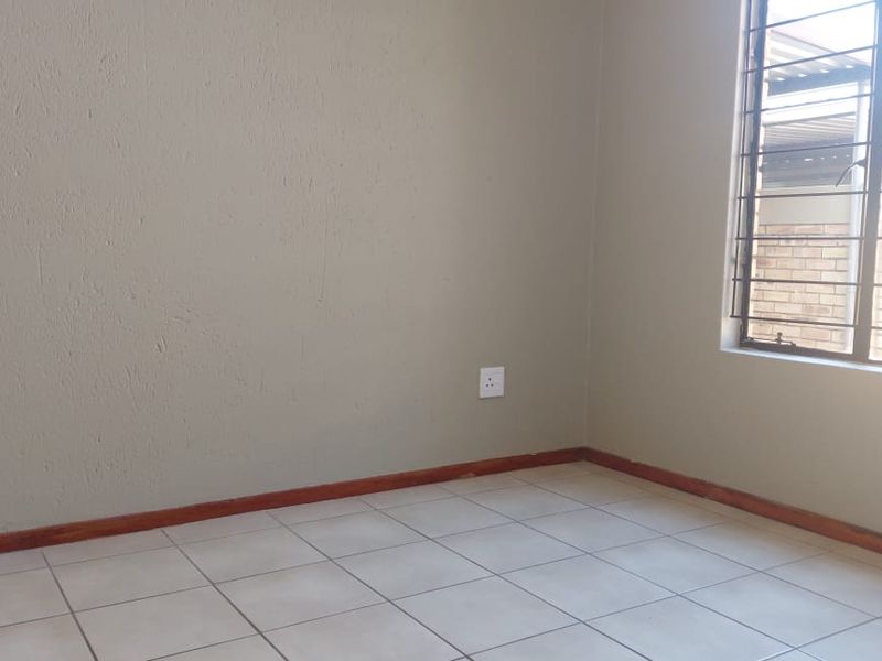 A vacant bedroom featuring neutral wall paint, tiled flooring, and a window fitted with security bars.