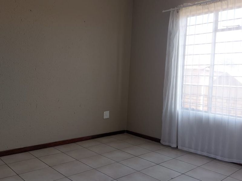 An empty bedroom featuring tiled flooring, neutral wall paint, and a window fitted with security bars.