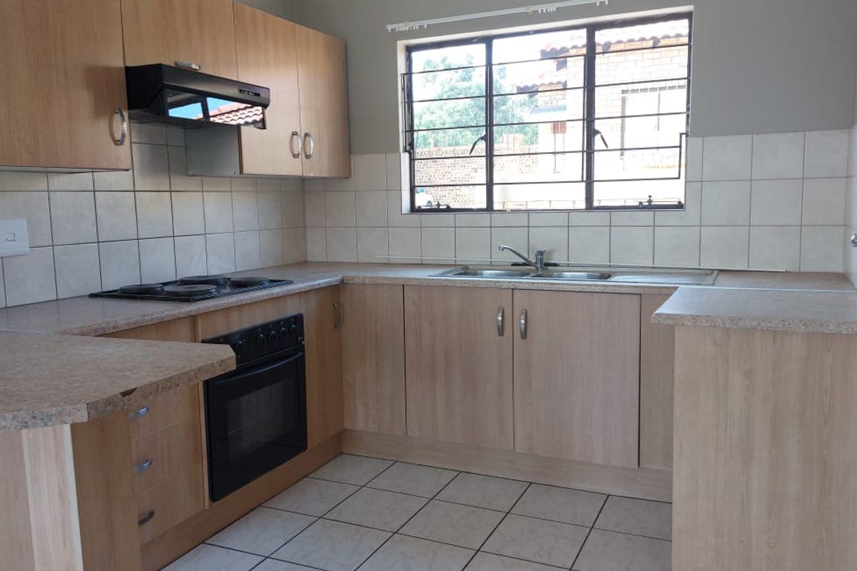 A functional kitchen featuring light wood-look cabinetry, laminate countertops, a built-in oven with hob, and tiled flooring with a neutral backsplash.