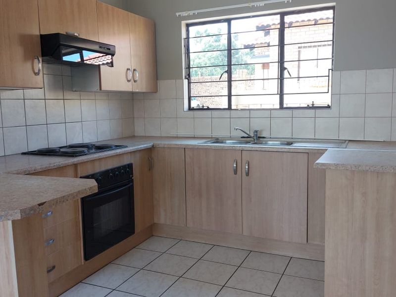 A functional kitchen featuring light wood-look cabinetry, laminate countertops, a built-in oven with hob, and tiled flooring with a neutral backsplash.