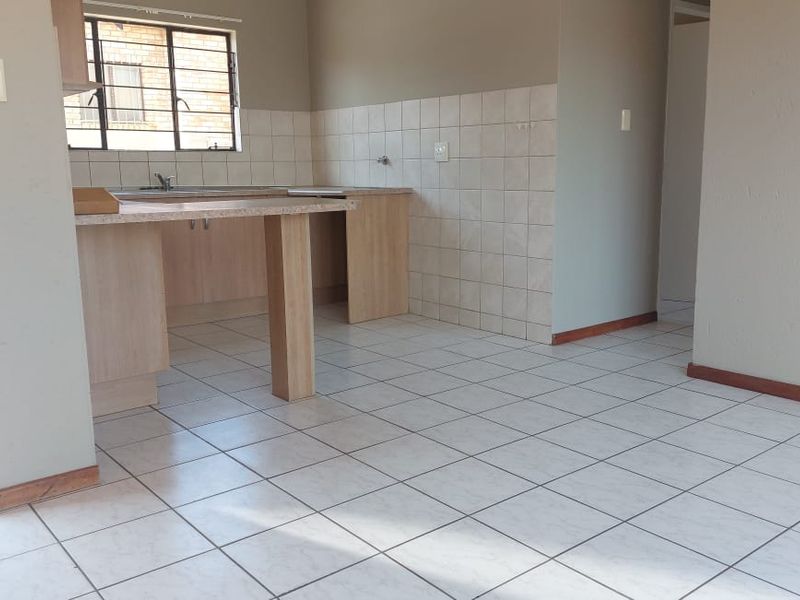 An empty, functional kitchen featuring laminate cabinetry, a stainless steel sink, and tiled flooring, offering a blank canvas for potential updates.