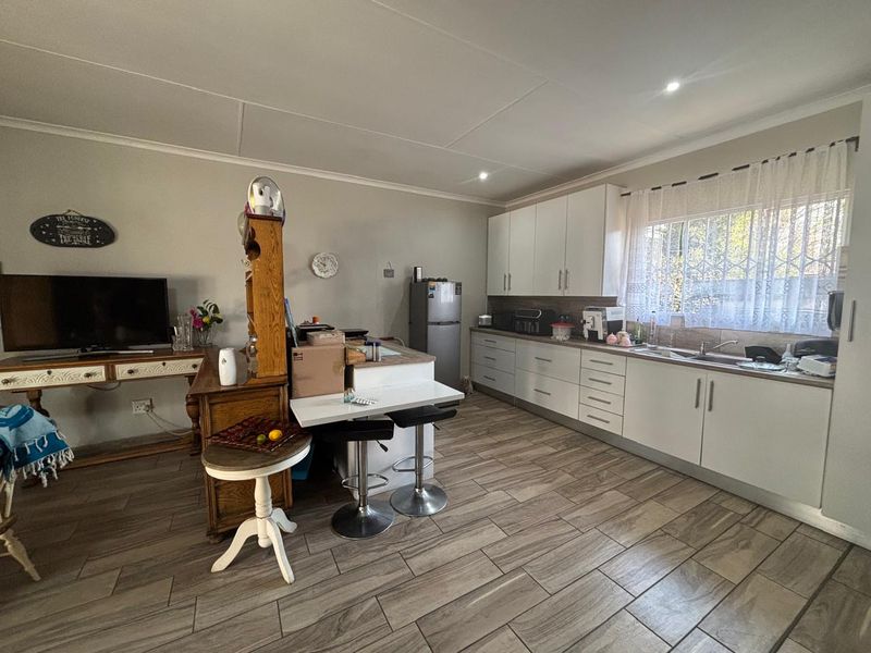 Open-plan kitchen and living area featuring modern white cabinetry, wood-look tile flooring, and ample natural light through a window with security bars.