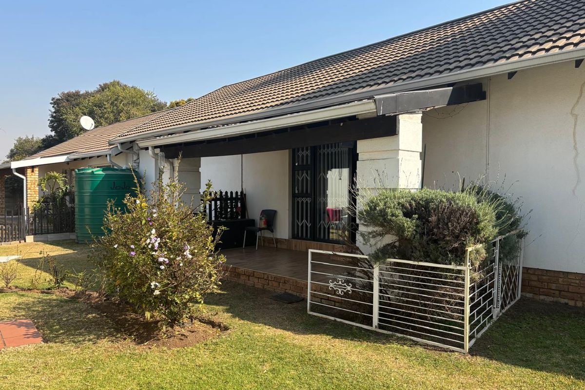 Rear view of the cottage featuring a covered patio, tiled roof, and a water storage tank set within a private garden area.