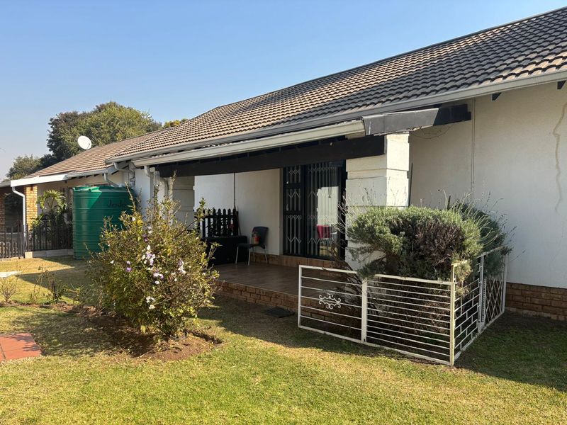 Rear view of the cottage featuring a covered patio, tiled roof, and a water storage tank set within a private garden area.