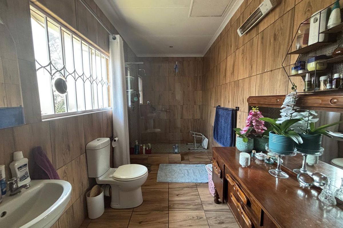 A functional bathroom featuring wood-look wall and floor tiles, a walk-in shower, pedestal basin, and a wall-mounted heater.
