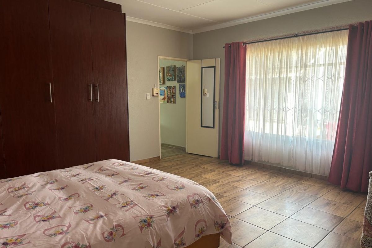A spacious bedroom featuring tiled flooring, a large built-in wardrobe, and a window fitted with a security gate.