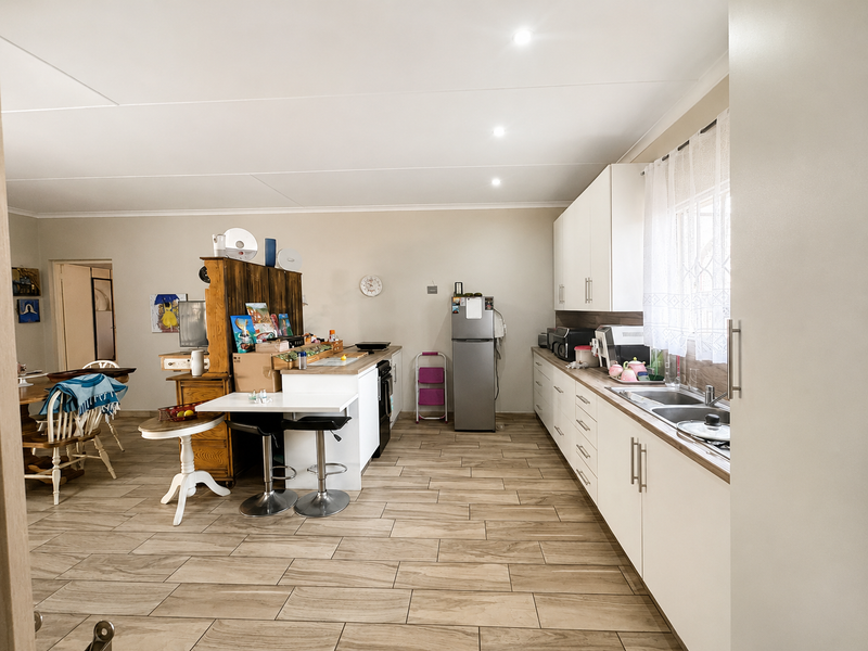 Spacious open-plan kitchen and living area featuring modern white cabinetry, a functional kitchen island, and durable wood-look tiled flooring throughout.