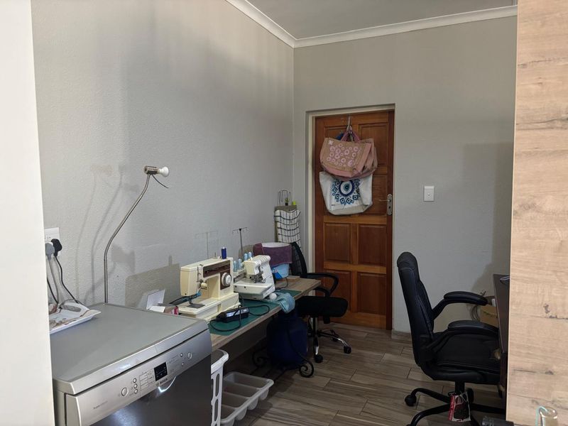 A functional utility space featuring tiled flooring, a built-in dishwasher, and a solid timber door, currently utilized as a workspace.