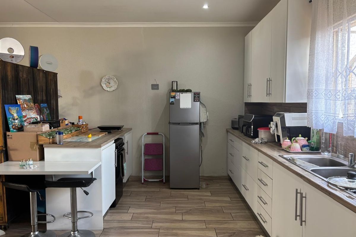 A functional kitchen featuring white cabinetry, wood-look laminate countertops, stainless steel sink, and tiled flooring with recessed lighting.