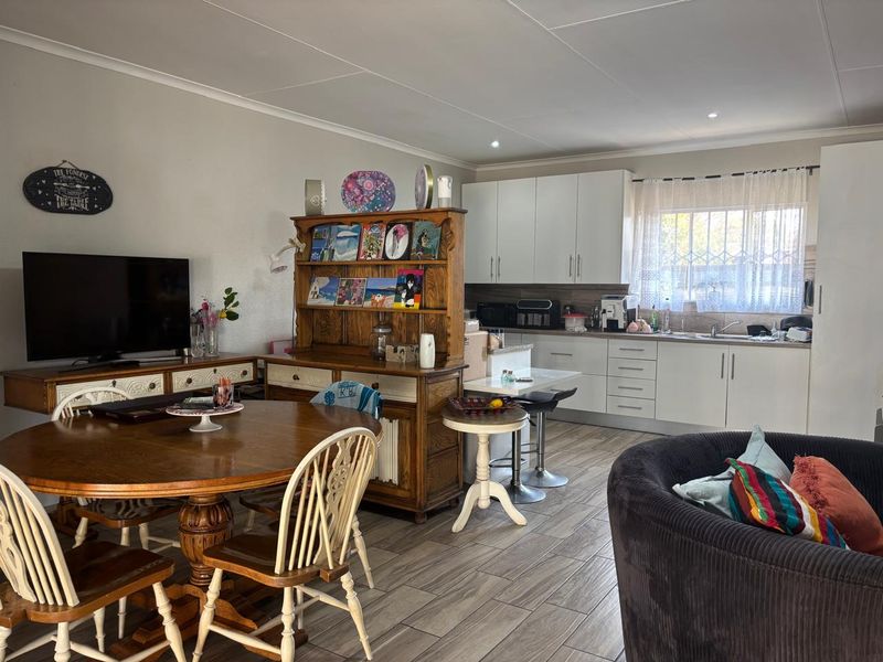 Open-plan living and kitchen area featuring modern white cabinetry, wood-look tiled flooring, and recessed lighting in a functional cottage layout.