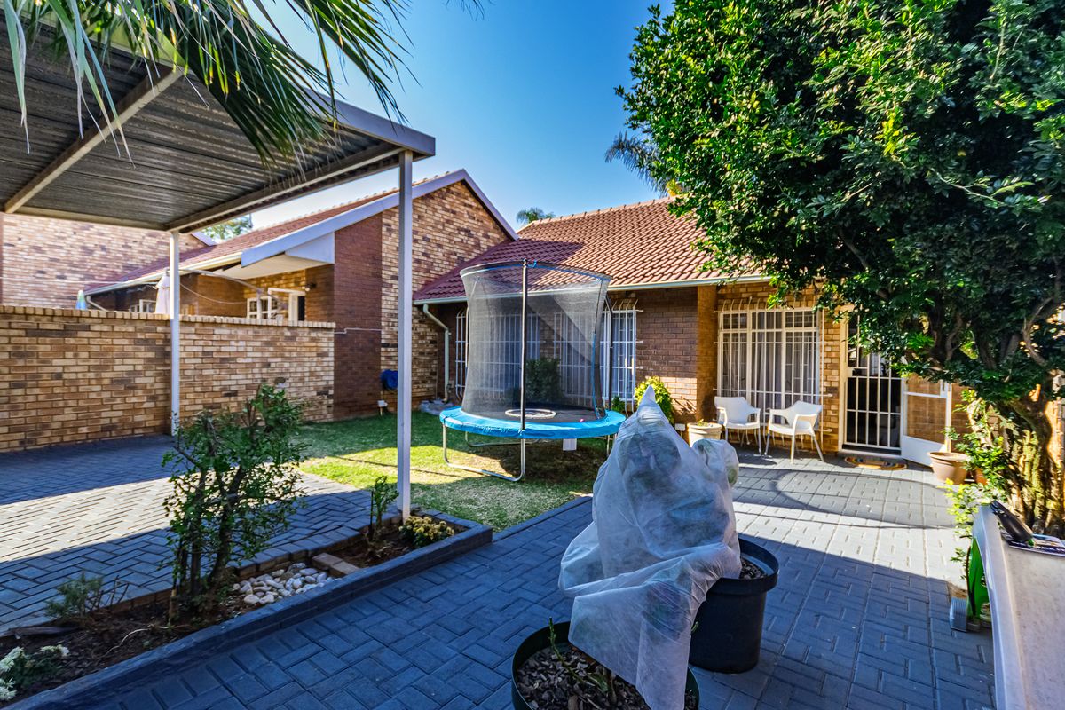 A private rear courtyard featuring brick paving, a covered patio area, and established garden surroundings, providing a functional outdoor space for the townhouse.