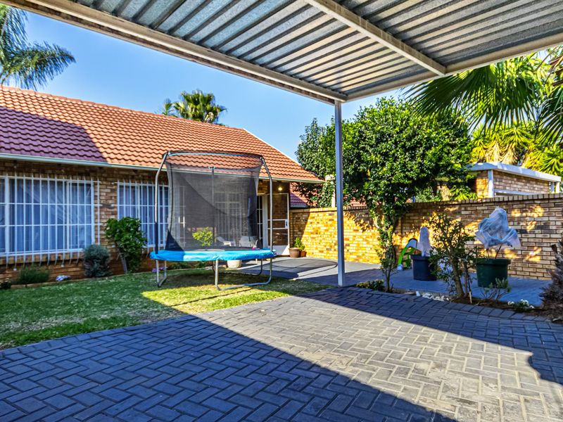 A covered patio area featuring brick paving, overlooking a private garden with a brick boundary wall and security-fitted windows on the main structure.