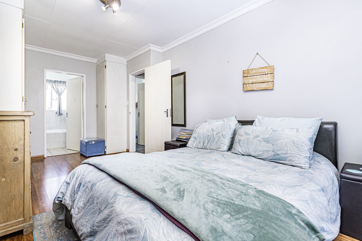 A well-lit bedroom featuring laminate flooring, built-in cupboards, and direct access to an adjoining bathroom.