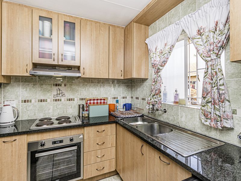 A functional kitchen featuring light wood-finish cabinetry, granite countertops, a built-in oven, electric hob, and a stainless steel sink with a window view.