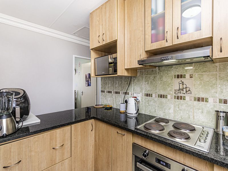 A functional kitchen featuring light wood cabinetry, granite countertops, a built-in oven, electric hob, and a decorative tiled backsplash.