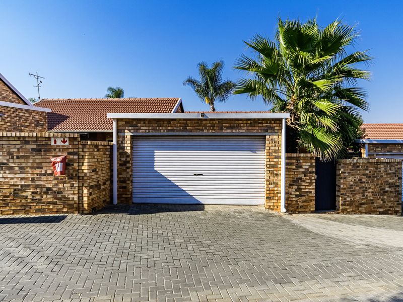 A well-maintained townhouse garage featuring a secure roller door, brick exterior finish, and a paved driveway area.