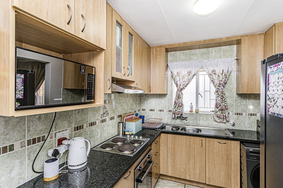 A functional kitchen featuring light wood cabinetry, granite countertops, a built-in oven, electric hob, and a tiled backsplash with a window view.