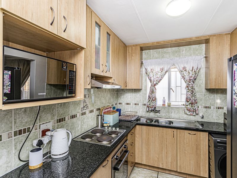 A functional kitchen featuring light wood cabinetry, granite countertops, a built-in oven, electric hob, and a tiled backsplash with a window view.