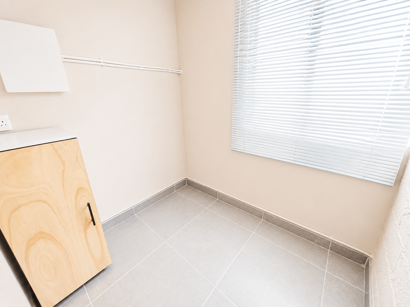 A clean, empty utility space featuring neutral tiled flooring, built-in cabinetry, and venetian blinds, suitable for a laundry or storage area.