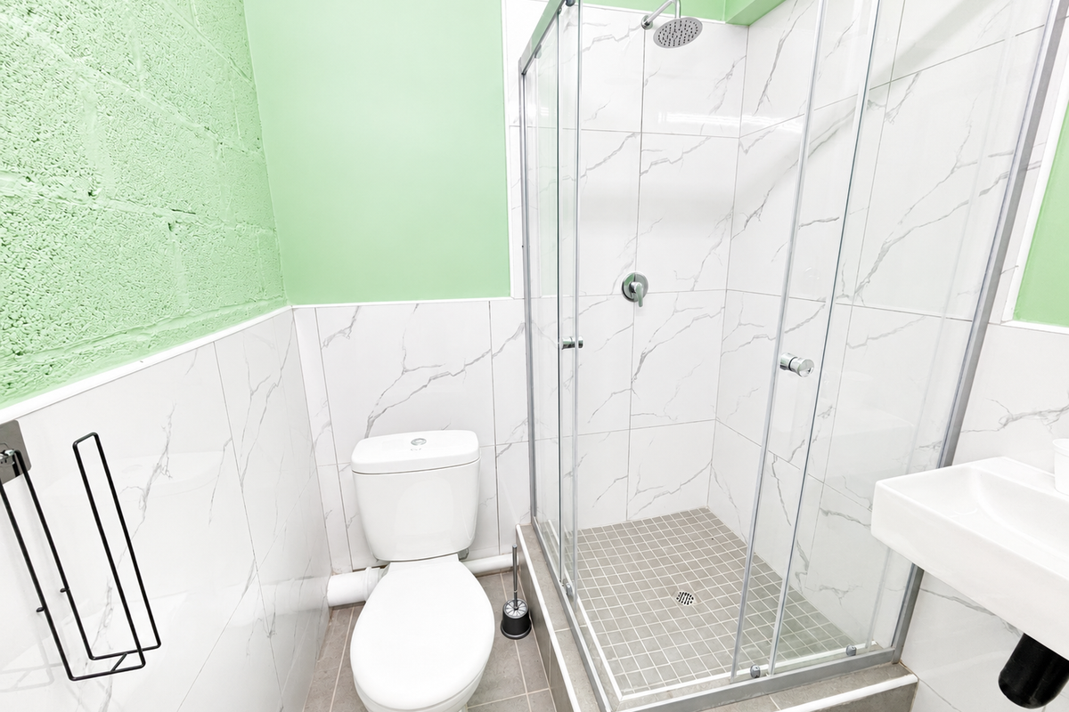 A clean, modern bathroom featuring a glass-enclosed shower, white toilet, and wall-mounted basin with marble-effect wall tiling and green painted accents.
