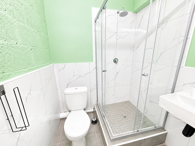 A clean, modern bathroom featuring a glass-enclosed shower, white toilet, and wall-mounted basin with marble-effect wall tiling and green painted accents.