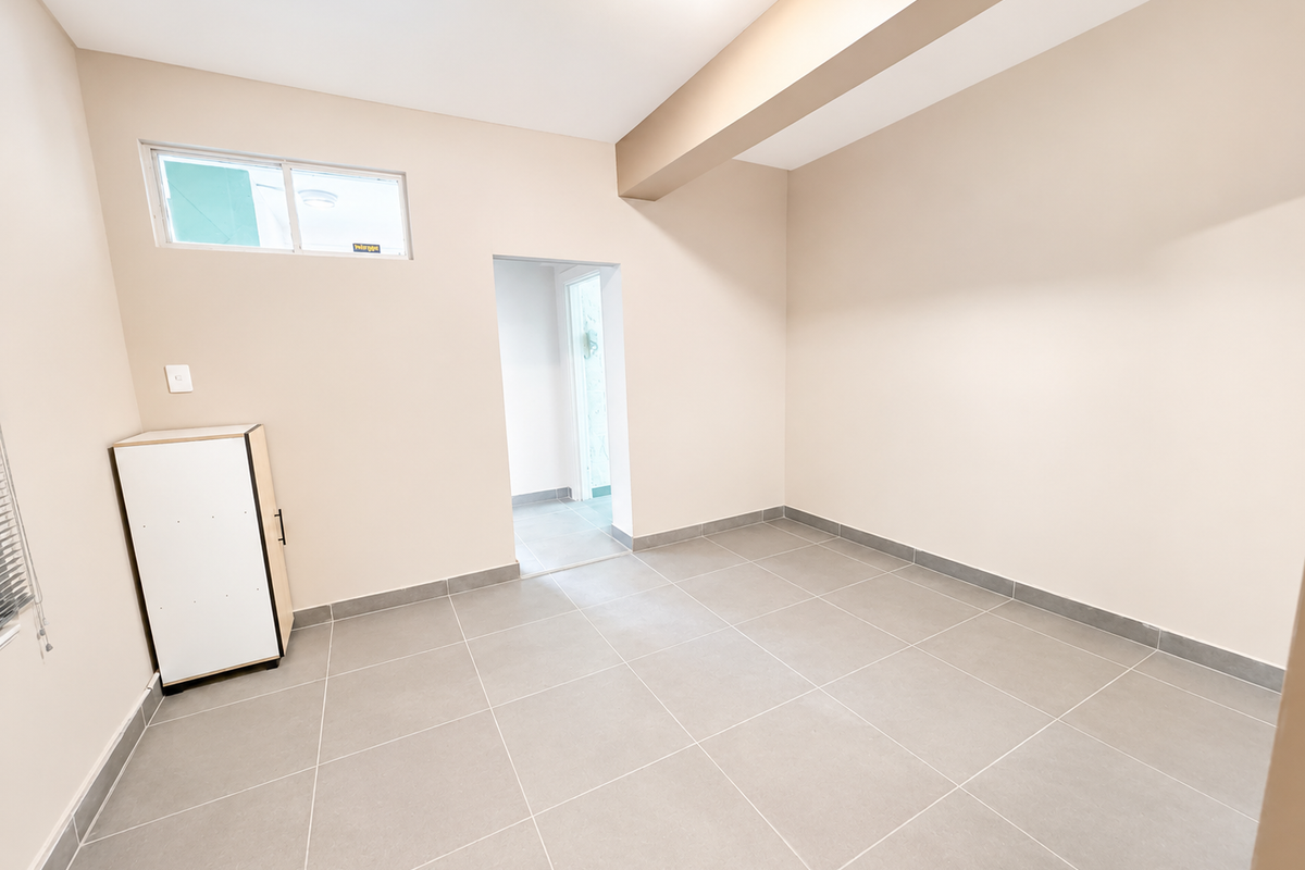 A bright, empty living area featuring neutral tiled flooring, clean walls, and a high-level window, providing a versatile blank canvas for interior design.