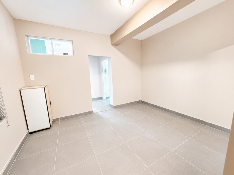 A bright, empty living area featuring neutral tiled flooring, clean walls, and a high-level window, providing a versatile blank canvas for interior design.