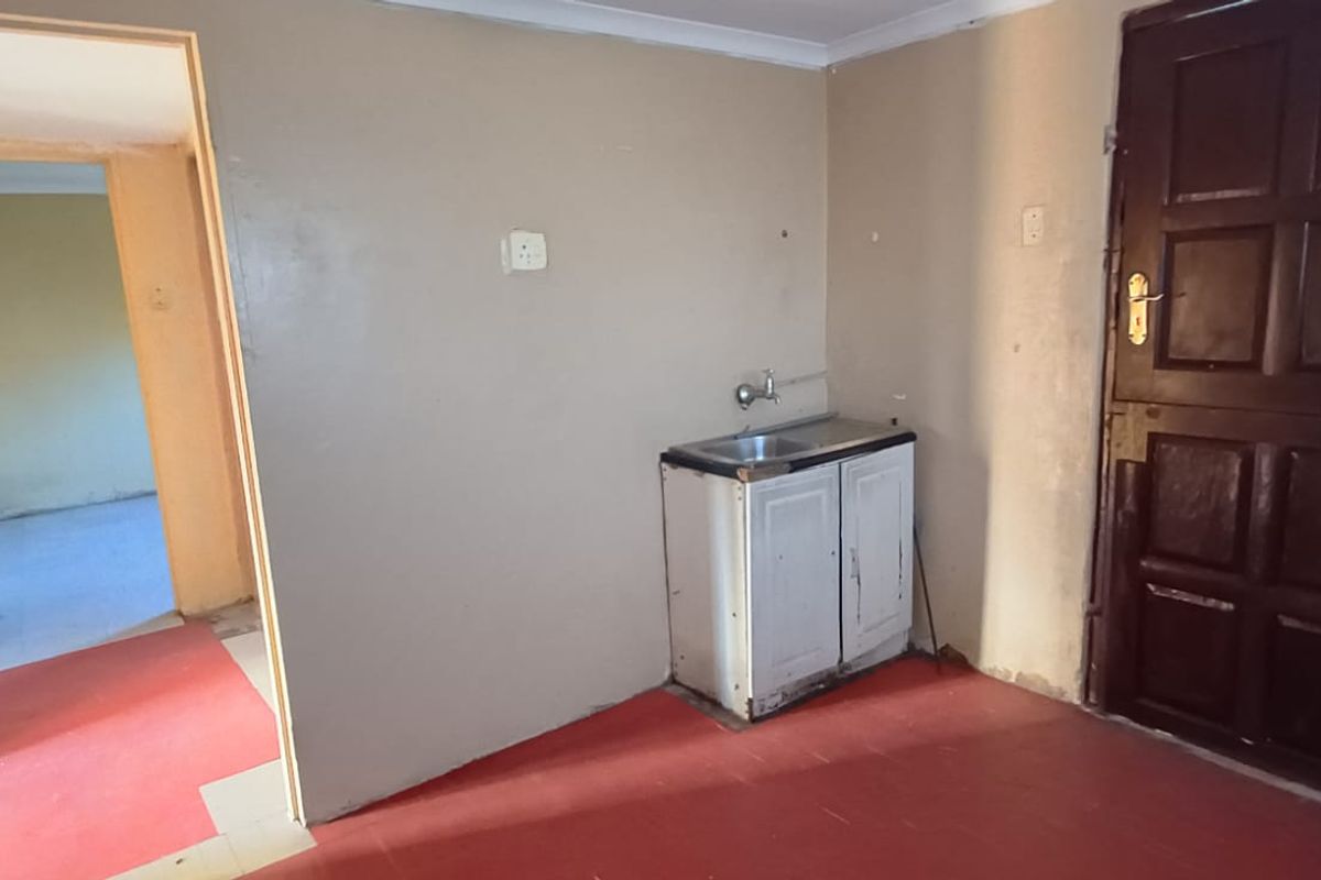 A basic, empty kitchen area featuring a small sink unit, tiled flooring, and access to an adjacent room.