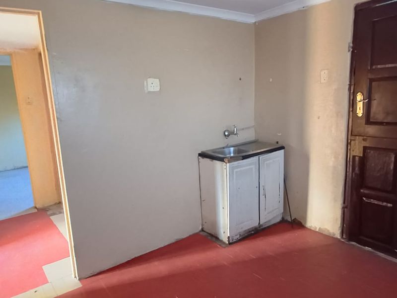 A basic, empty kitchen area featuring a small sink unit, tiled flooring, and access to an adjacent room.