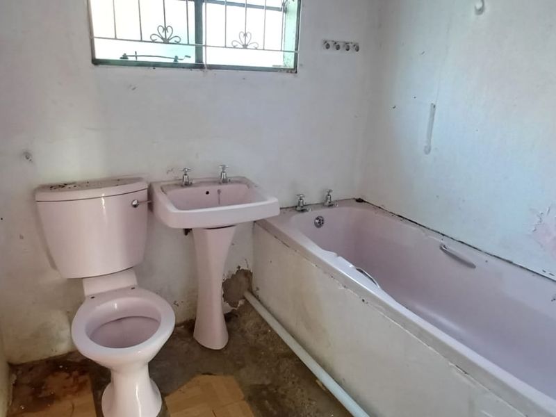 A dated bathroom featuring a pink suite including a pedestal basin, toilet, and bathtub, requiring significant renovation and cosmetic updates.
