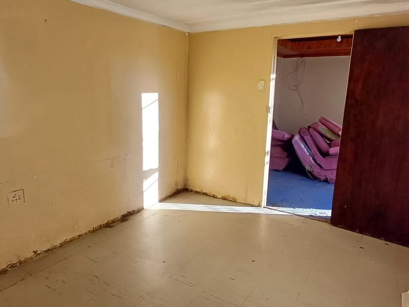 A vacant bedroom featuring tiled flooring and a wooden door, requiring cosmetic updates and wall repairs to restore its condition.