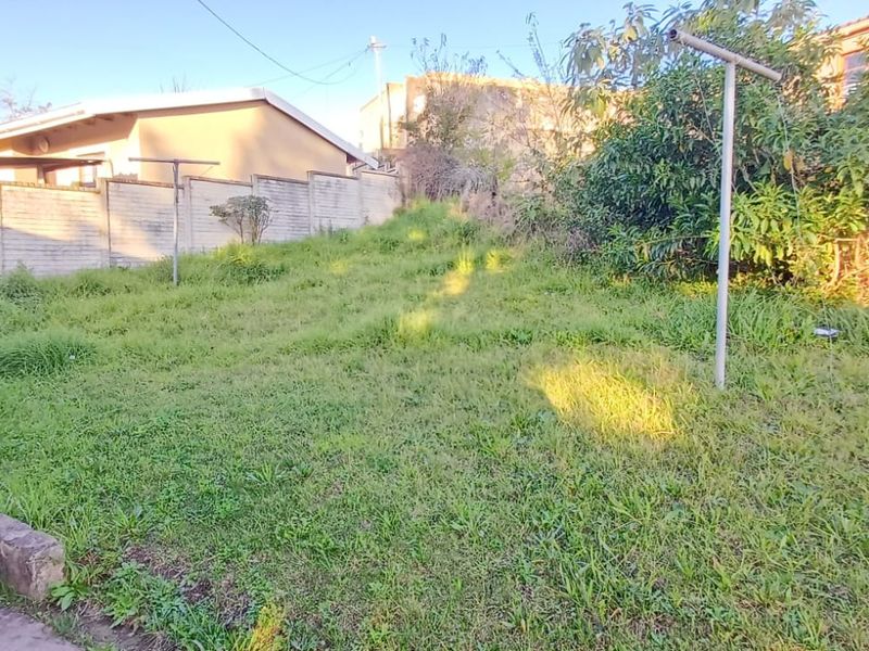A rear garden area featuring a sloped lawn, brick boundary wall, and concrete retaining edge, requiring landscaping and maintenance.