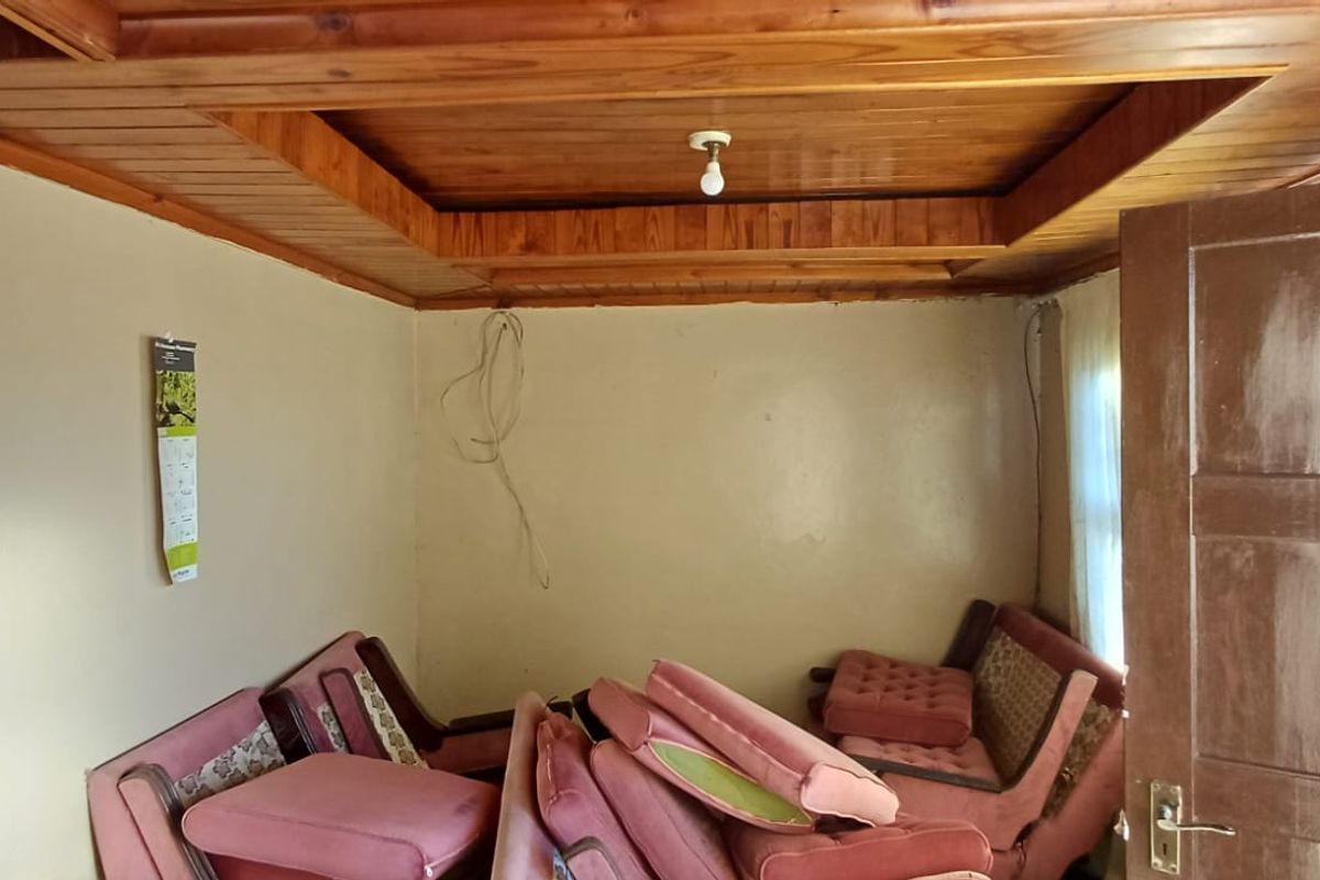 A living room featuring a distinctive timber-clad tray ceiling and a solid timber door, requiring cosmetic updates to the walls and electrical fixtures.