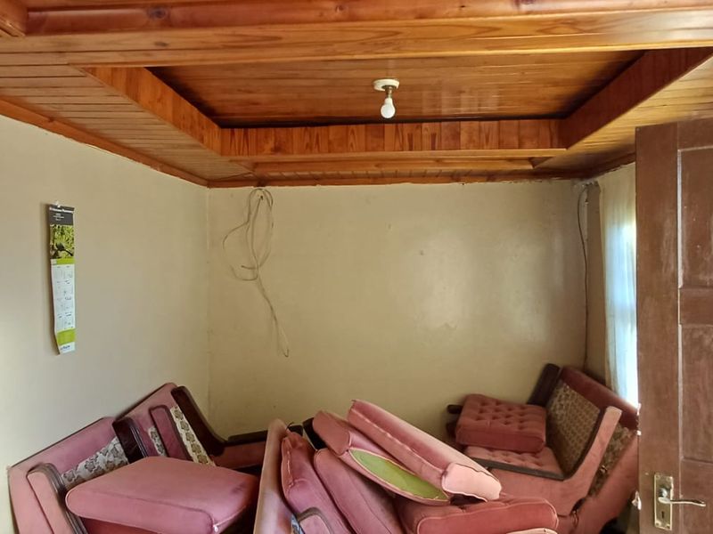 A living room featuring a distinctive timber-clad tray ceiling and a solid timber door, requiring cosmetic updates to the walls and electrical fixtures.