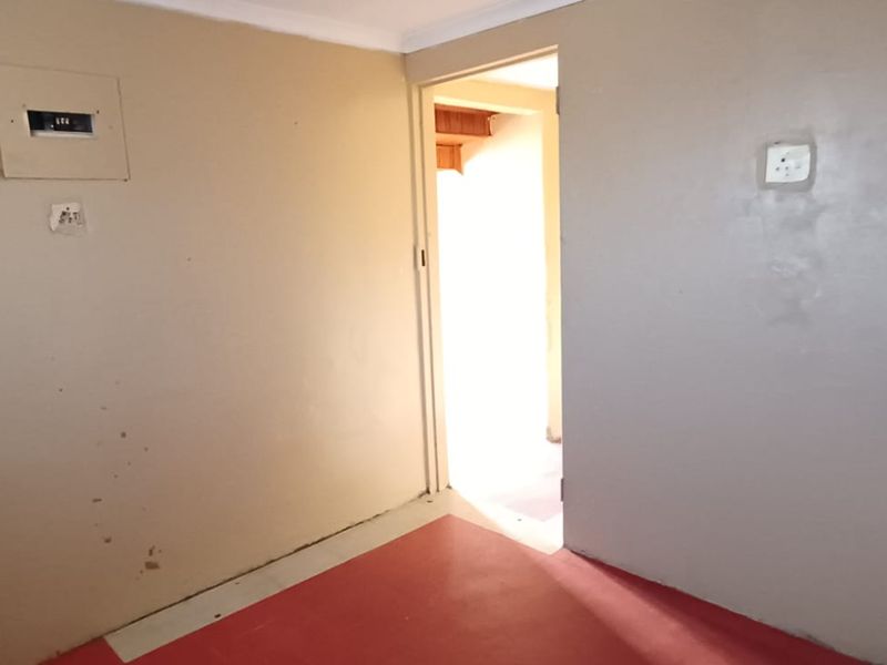 A utility space featuring a built-in sink, electrical distribution board, and alarm system keypad, with painted walls and a red floor finish.