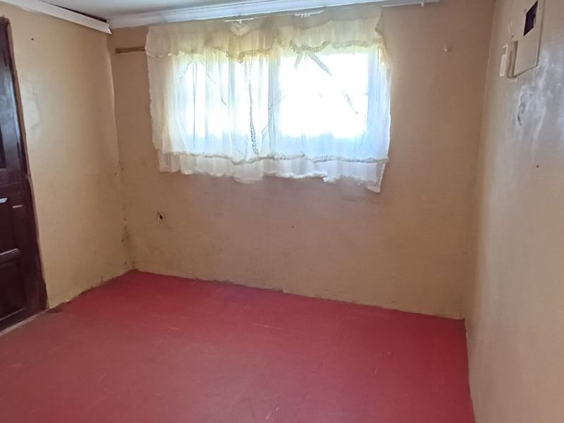 An empty bedroom featuring a timber door, a window, and an electrical distribution board, requiring cosmetic updates to the walls and flooring.