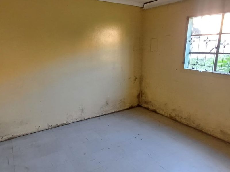 An empty bedroom featuring tiled flooring and a window with security bars, requiring cosmetic updates and wall repairs.