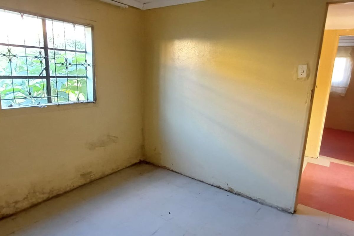 An empty bedroom featuring tiled flooring and a window with security bars, showing signs of wear and requiring cosmetic updates.