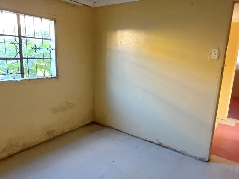 An empty bedroom featuring tiled flooring and a window with security bars, showing signs of wear and requiring cosmetic updates.