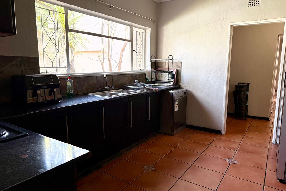 A functional kitchen featuring dark cabinetry, laminate countertops, a double sink, and tiled flooring with natural light from a large window.