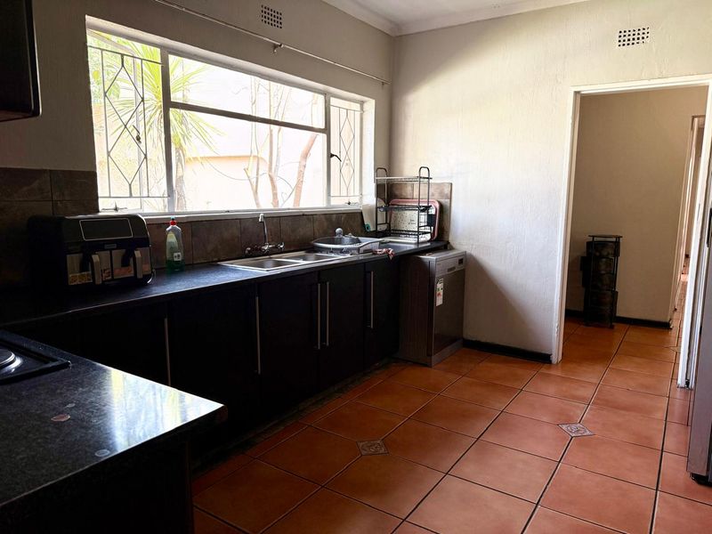 A functional kitchen featuring dark cabinetry, laminate countertops, a double sink, and tiled flooring with natural light from a large window.
