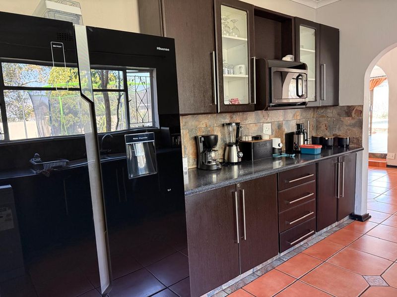 A functional kitchen featuring dark wood cabinetry, stone tile backsplash, laminate countertops, and ceramic floor tiles, with a view into the adjacent outdoor area.