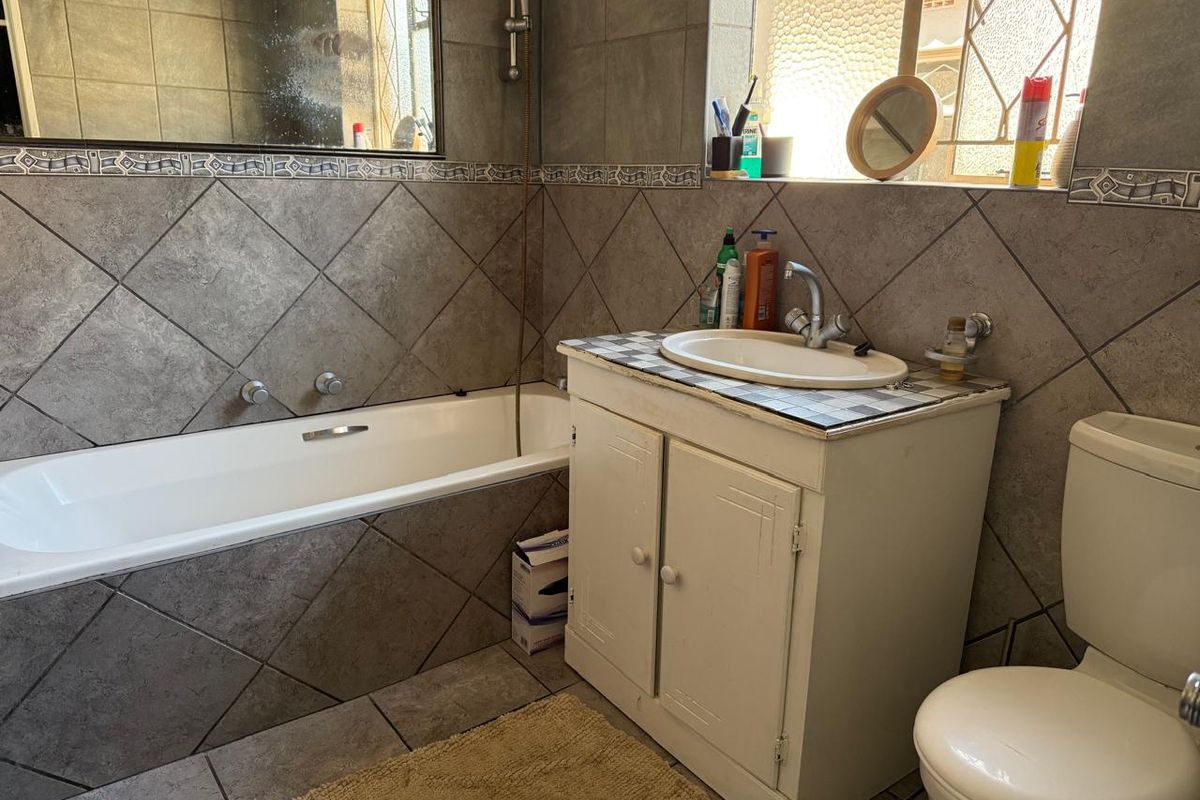 A functional bathroom featuring a built-in bathtub, a vanity cabinet with a basin, and a toilet, finished with neutral wall and floor tiles.