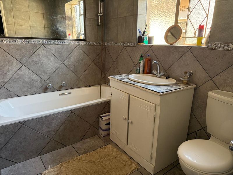 A functional bathroom featuring a built-in bathtub, a vanity cabinet with a basin, and a toilet, finished with neutral wall and floor tiles.