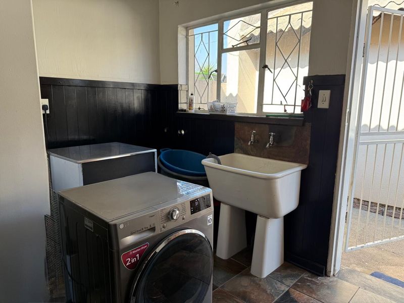 Functional laundry area featuring a ceramic utility sink, tiled flooring, and direct access to the exterior via a security gate.
