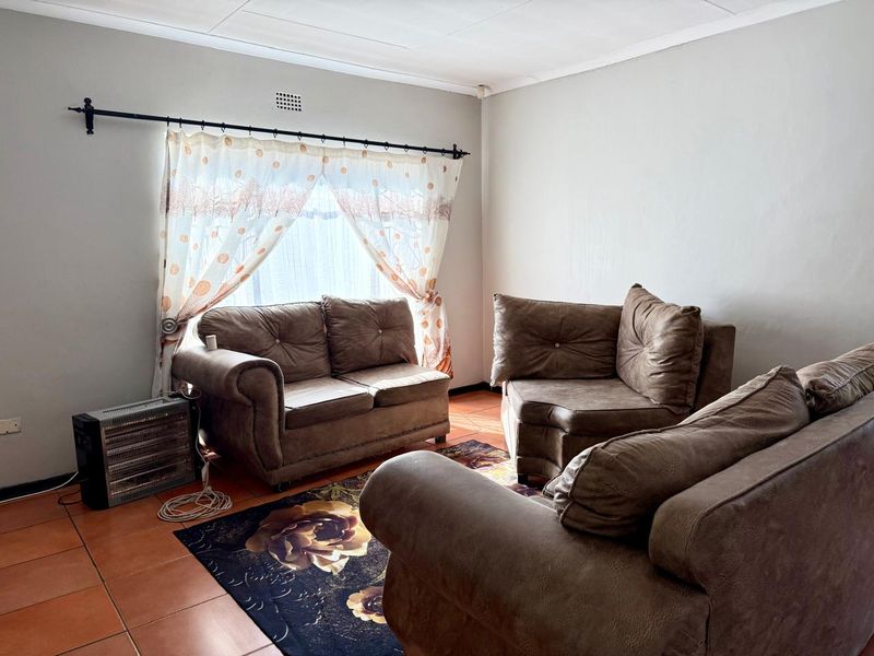 A living room featuring terracotta floor tiles and a window with a curtain rod.