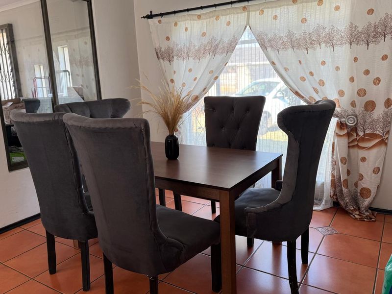 A dining area featuring terracotta floor tiles and a window with a curtain rod, providing a functional space for meals.